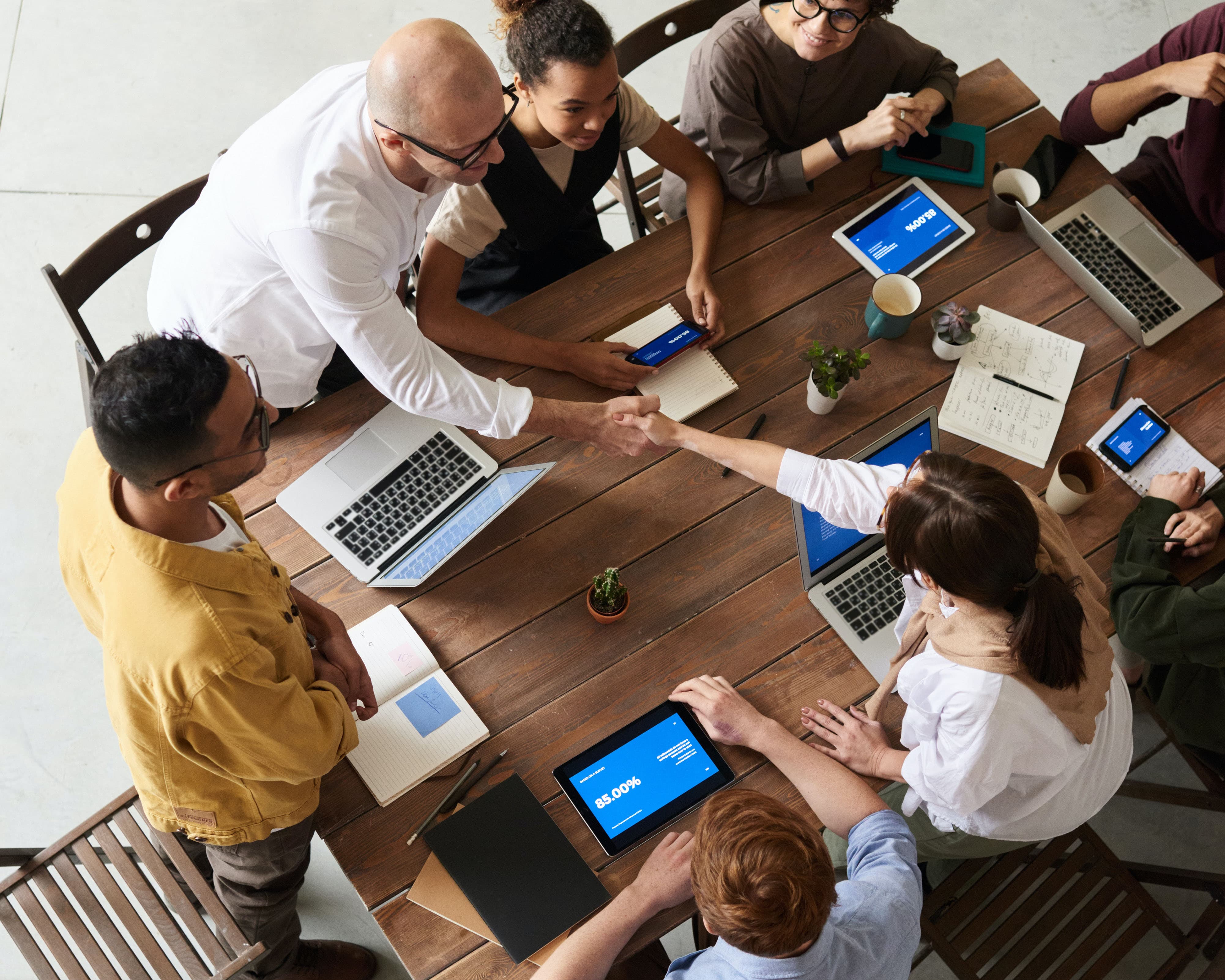 New coworkers shaking hands over a table in a meeting after agency merger