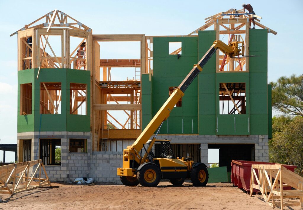 Partially constructed house with wooden framing and green sheathing, supported by a telescopic crane—representing the construction aspect of COPE in insurance.