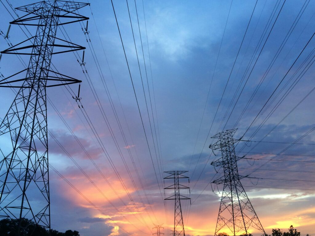 High-voltage power lines silhouetted against a colorful sunset sky—representing infrastructure exposure in property insurance risk assessment.